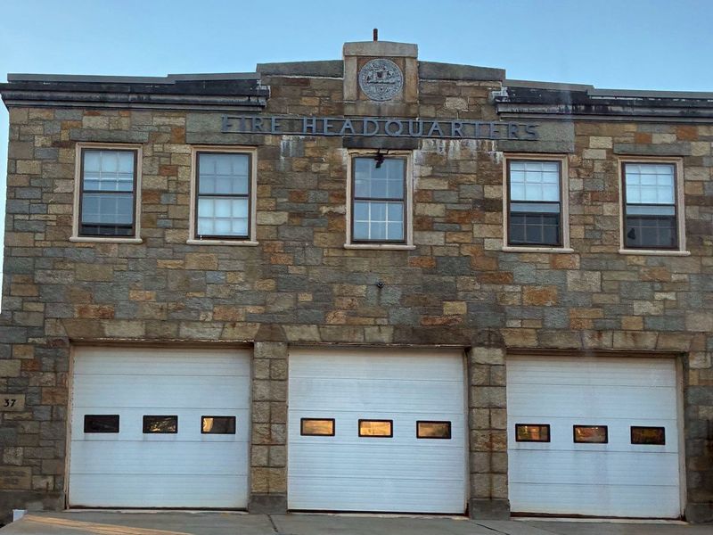 The granite Fire Headquarters building on Broadway in Rockport, with the town seal over its sign and three white garage doors