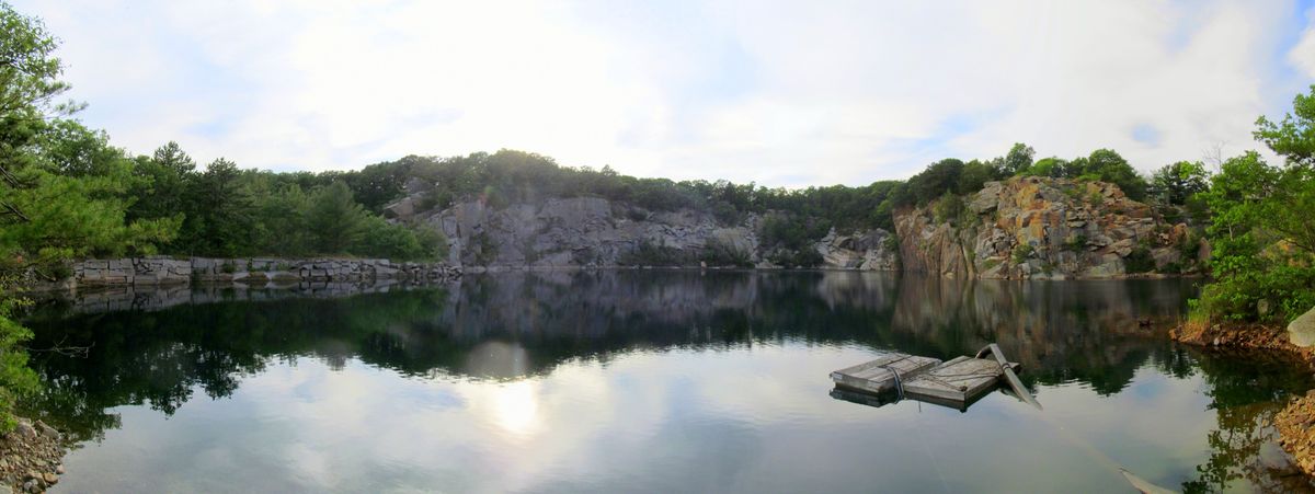 Panorama de Flat Ledge Quarry rodeada de salientes de granito y árboles, con una toma de bomba flotante sobre el agua